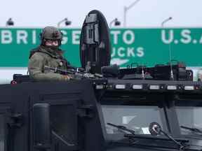 Un officier tactique de la Police provinciale de l'Ontario regarde depuis la trappe supérieure d'un véhicule blindé alors que les manifestants se préparent à partir avant que la police n'applique une injonction contre leur manifestation, qui a bloqué la circulation sur le pont Ambassador par des manifestants contre les restrictions du COVID-19, à Windsor , Ont., samedi 12 février 2022.