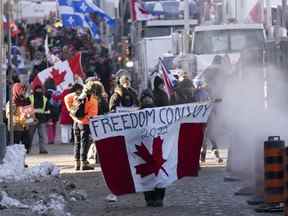 Des manifestants participant à un convoi de camions à travers le pays protestant contre les mesures prises par les autorités pour freiner la propagation de la COVID-19 et les mandats de vaccination marchent près de la Colline du Parlement à Ottawa.