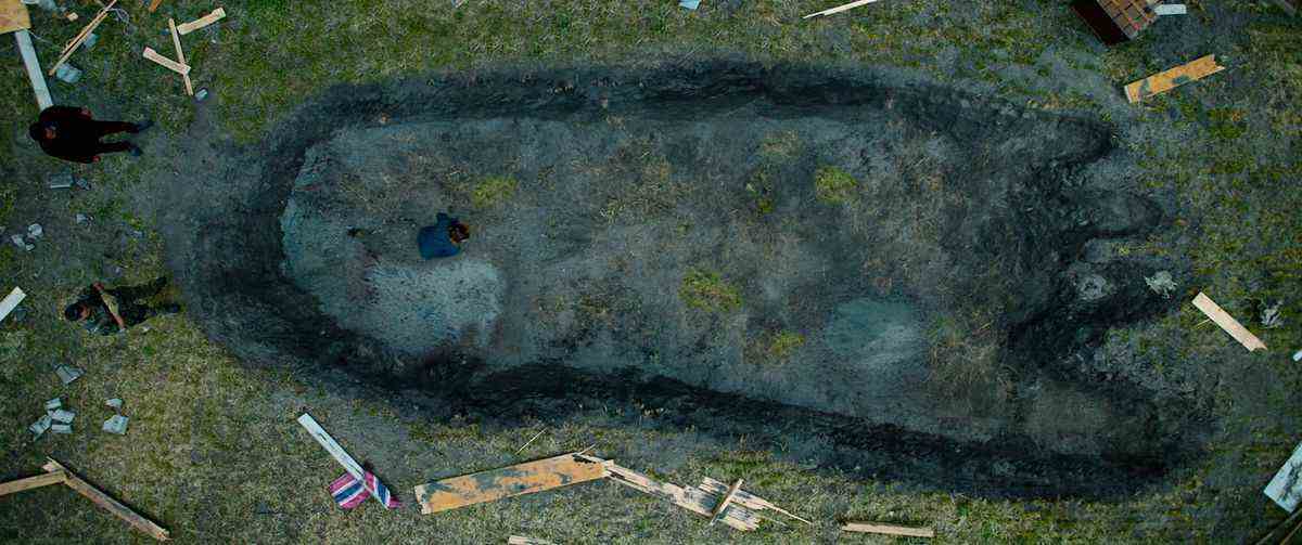 Une photo de haut en bas d'une immense empreinte de pas de troll enfoncée profondément dans un champ herbeux, avec de minuscules figures humaines l'examinant de côté, dans le Troll 2022