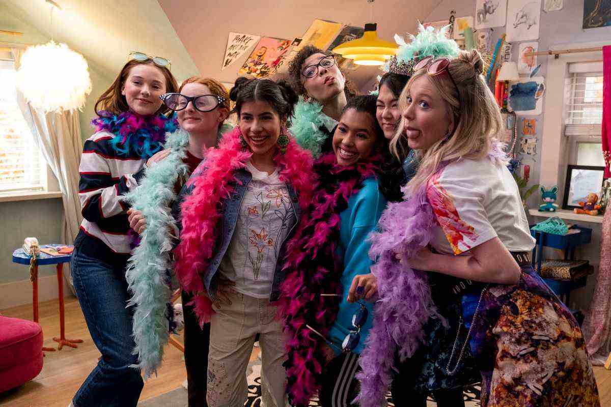 Un groupe d'adolescentes portant des boas de plumes colorés et des lunettes surdimensionnées riant, tirant la langue et posant pour des photos.