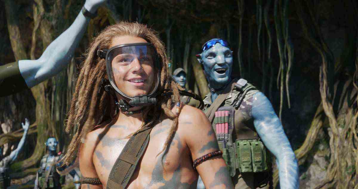 un jeune garçon blanc avec des dreadlocks portant un masque clair en avatar : la voie de l'eau.  derrière lui se trouvent des na'vi bleus en tenue de commando. 