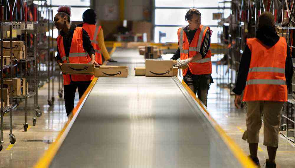 Des travailleurs d'Amazon chargent des cartons sur un tapis roulant dans un entrepôt en France.