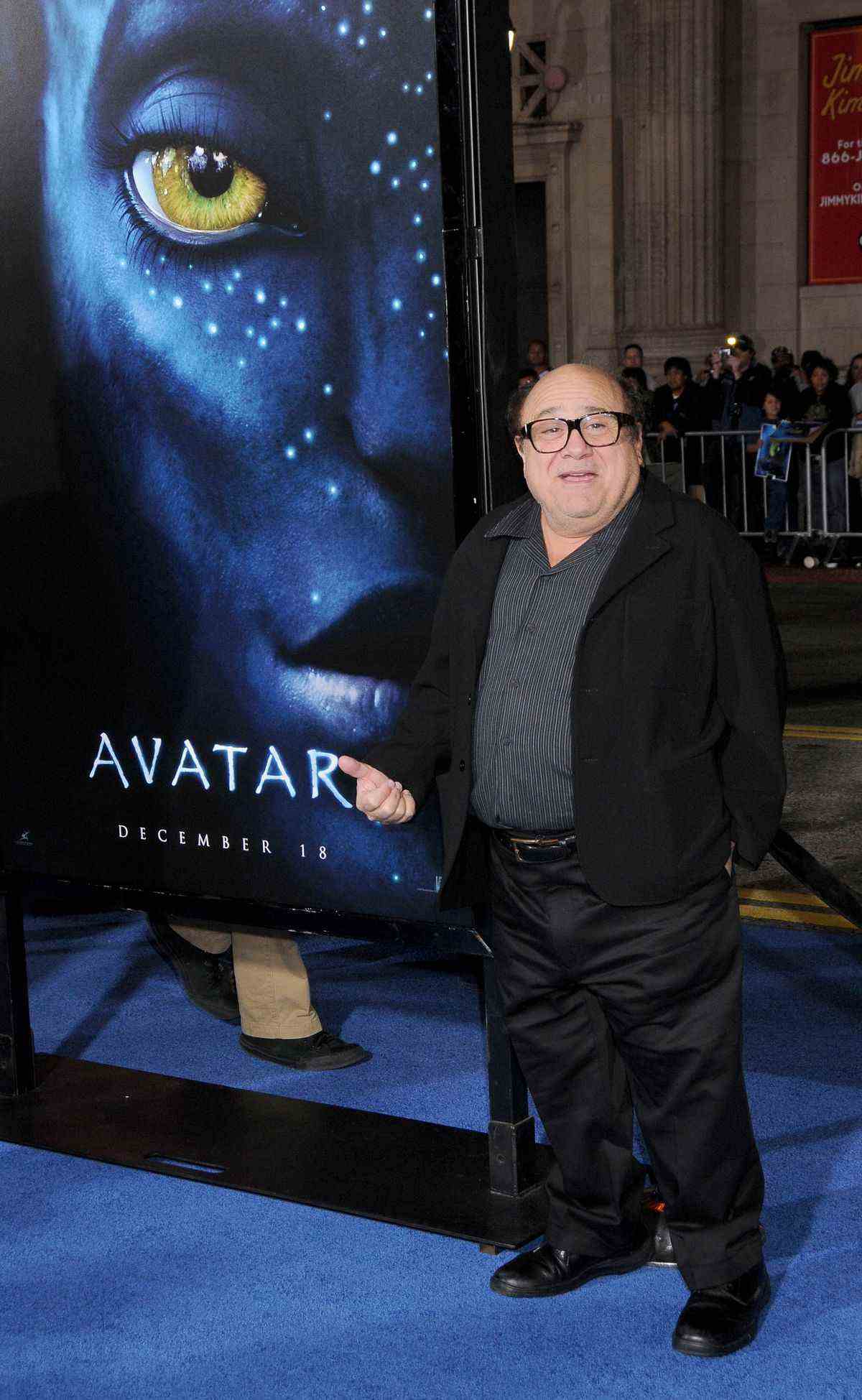 Danny DeVito se tenant à nouveau à côté d'une affiche d'Avatar disant peut-être 