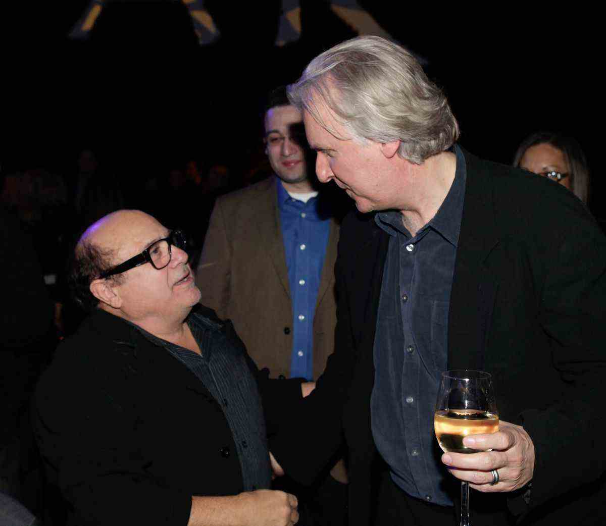 Danny Devito lève les yeux pour parler au réalisateur James Cameron, qui tient un verre de vin blanc à l'after party d'Avatar