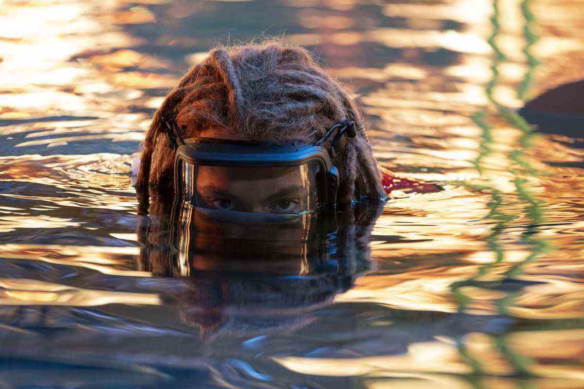 Araignée (Jack Champion) portant un masque à oxygène alors qu'il sort de l'eau, qui scintille de reflets de feu dans Avatar: The Way of Water