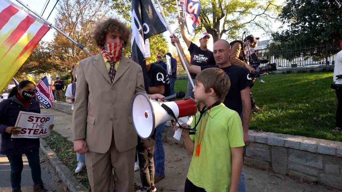 Andrew Callaghan interviewe un petit enfant avec un mégaphone, entouré de manifestants, dans This Place Rules