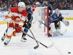 Mikael Backlund des Calgary Flames, à gauche, et Boone Jenner des Blue Jackets de Columbus poursuivent la rondelle alors que Joonas Korpisalo (70 ans) des Blue Jackets protège le filet pendant la première période d'un match de hockey de la LNH le vendredi 9 décembre 2022 à Columbus , Ohio.