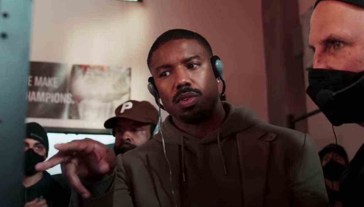 Michael B. Jordan pointing at a monitor and wearing headphones while directing Creed III