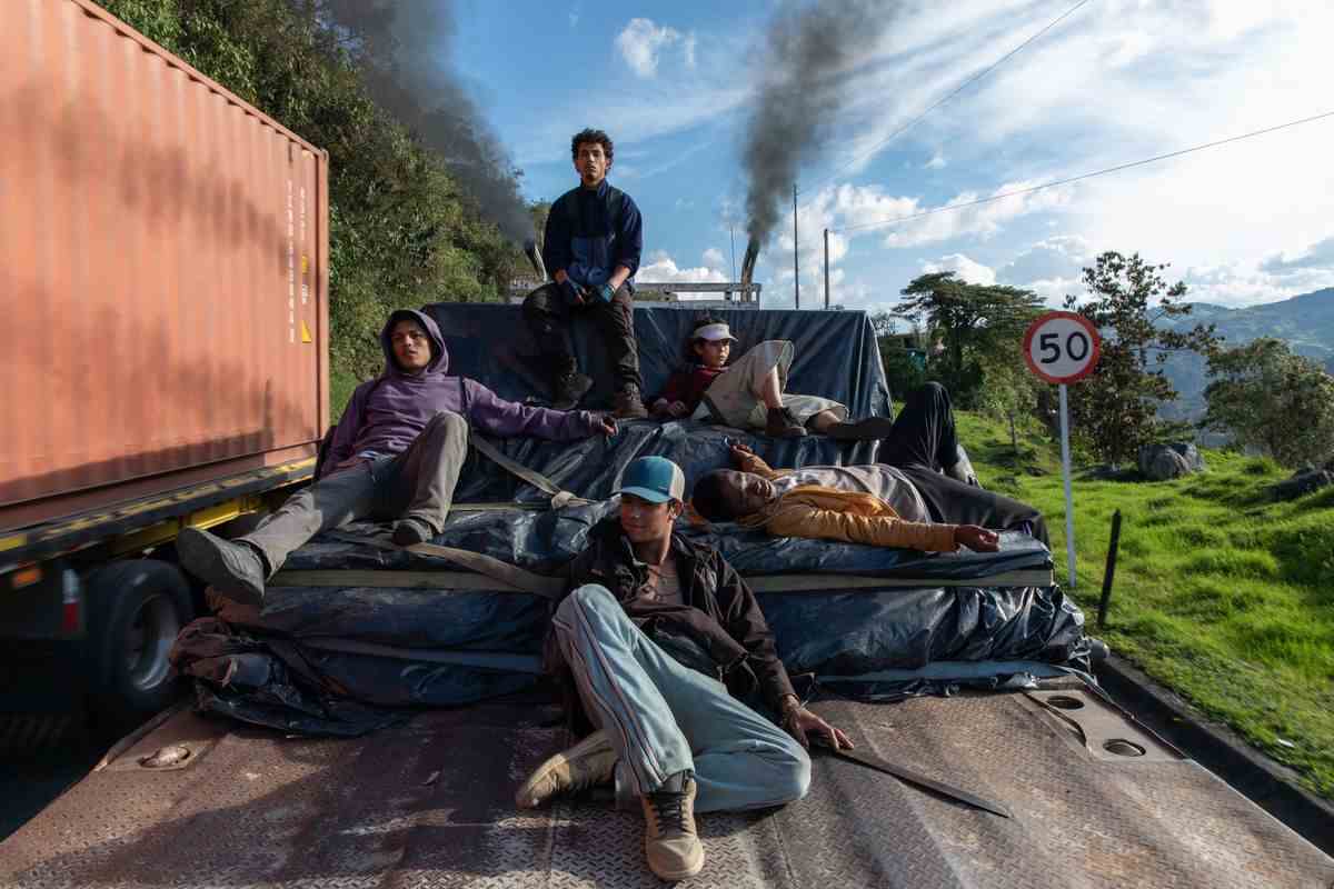 Cinq garçons (Carlos Andrés Castañeda, Davison Florez, Brahian Acevedo, Cristian Campaña, Cristian David Duque) sont assis au sommet d'un monticule de bâches sur le lit d'un wagon flanqué d'arbres, d'un conteneur de stockage orange et d'un ciel bleu en arrière-plan.