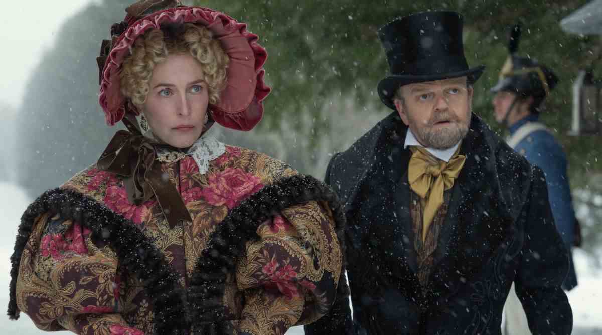 Gillian Anderson dans une enveloppe et un bonnet de brocart incroyablement volumineux et Toby Jones dans un haut-de-forme et un costume se tiennent dans la neige en tant que Julia et le Dr Marquis dans The Pale Blue Eye