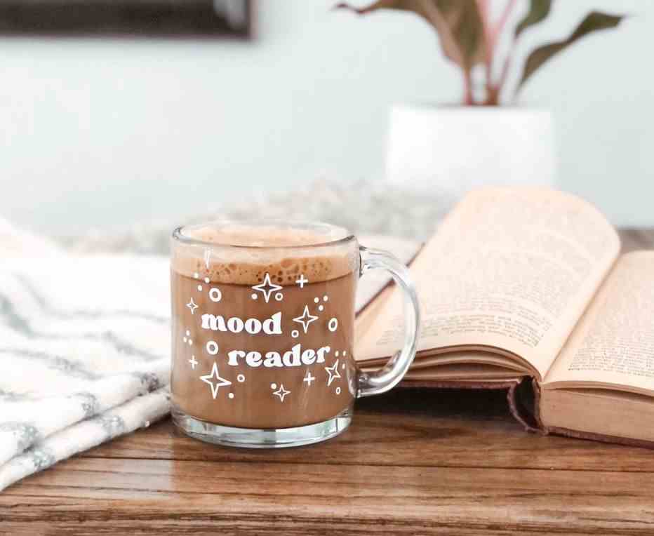 Image d'une tasse en verre sur une table avec un livre ouvert.  En blanc sur la tasse sont les mots 