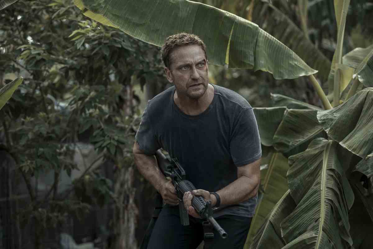 Brodie de Gerard Butler, saignant du côté gauche de son visage, traverse la jungle avec son arme dans Avion