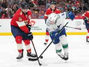 L'ailier droit des Canucks de Vancouver Conor Garland (8) et le défenseur des Panthers de la Floride Aaron Ekblad (5) se battent pour la rondelle lors de la première période au FLA Live Arena le 14 janvier 2023.