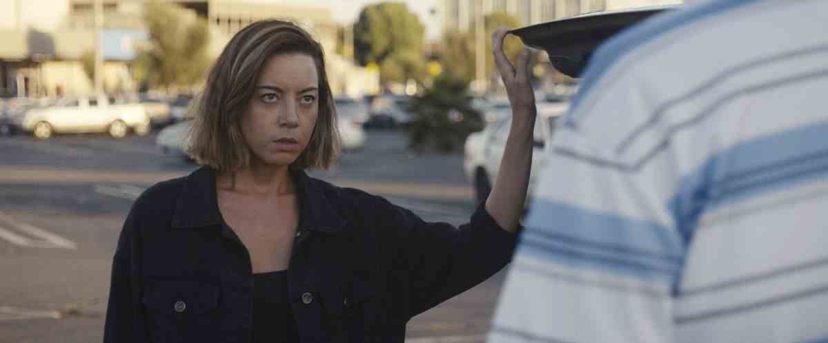 Aubrey Plaza alors qu'Emily se tient près de son coffre de voiture, regardant un acheteur potentiel dans Emily the Criminal