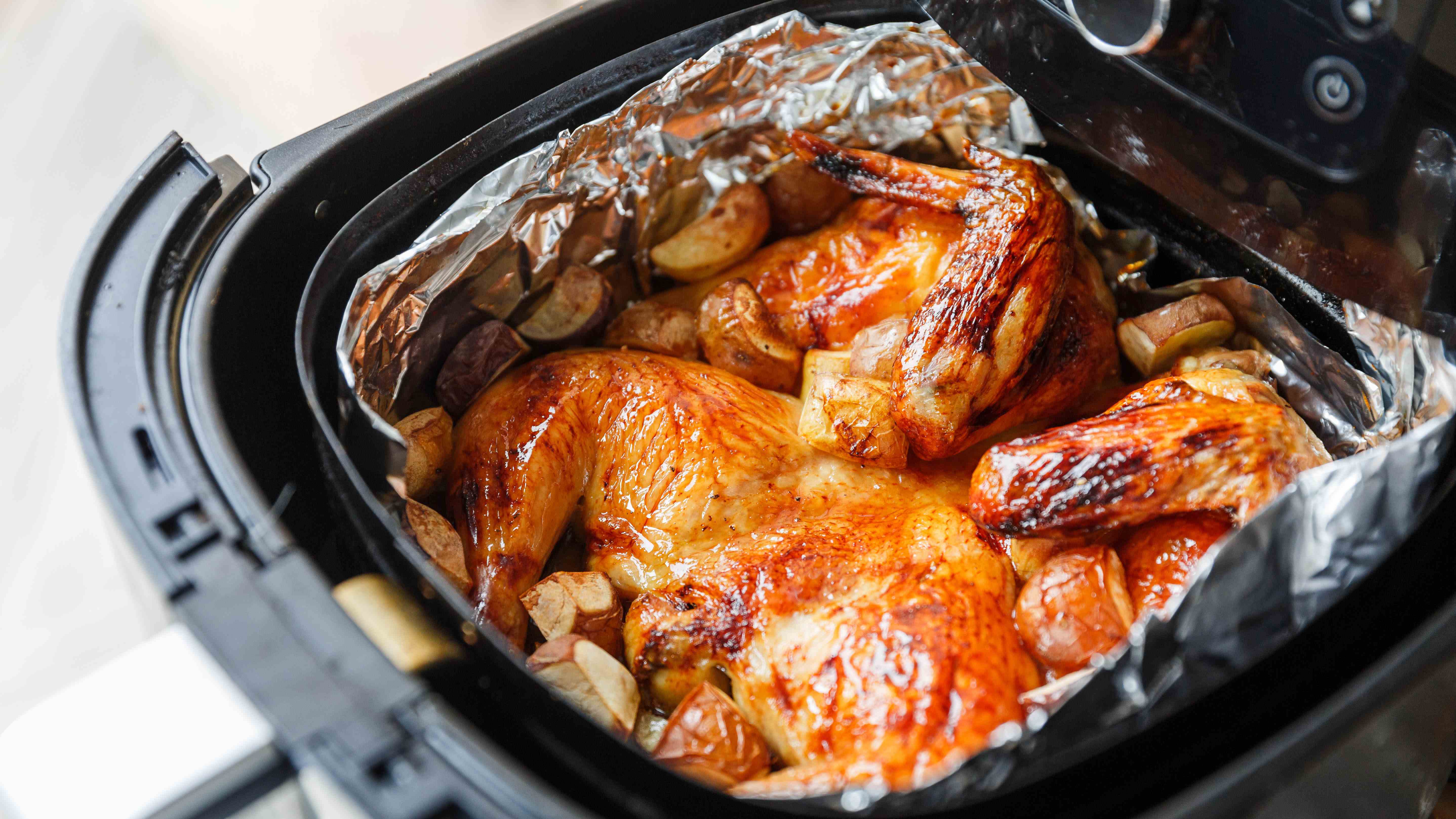 Un poulet avec des pommes de terre dans un panier de friteuse à air