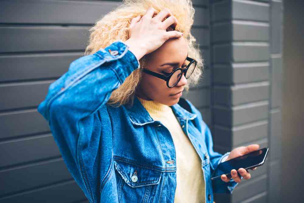 Jeune femme regardant le téléphone et saisissant les cheveux de frustration.