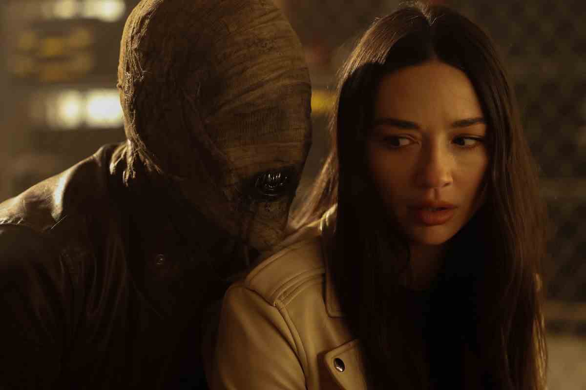 Une momie grognant aux dents ensanglantées se glisse derrière Crystal Reed dans le rôle d'Allison Argent dans TEEN WOLF : LE FILM