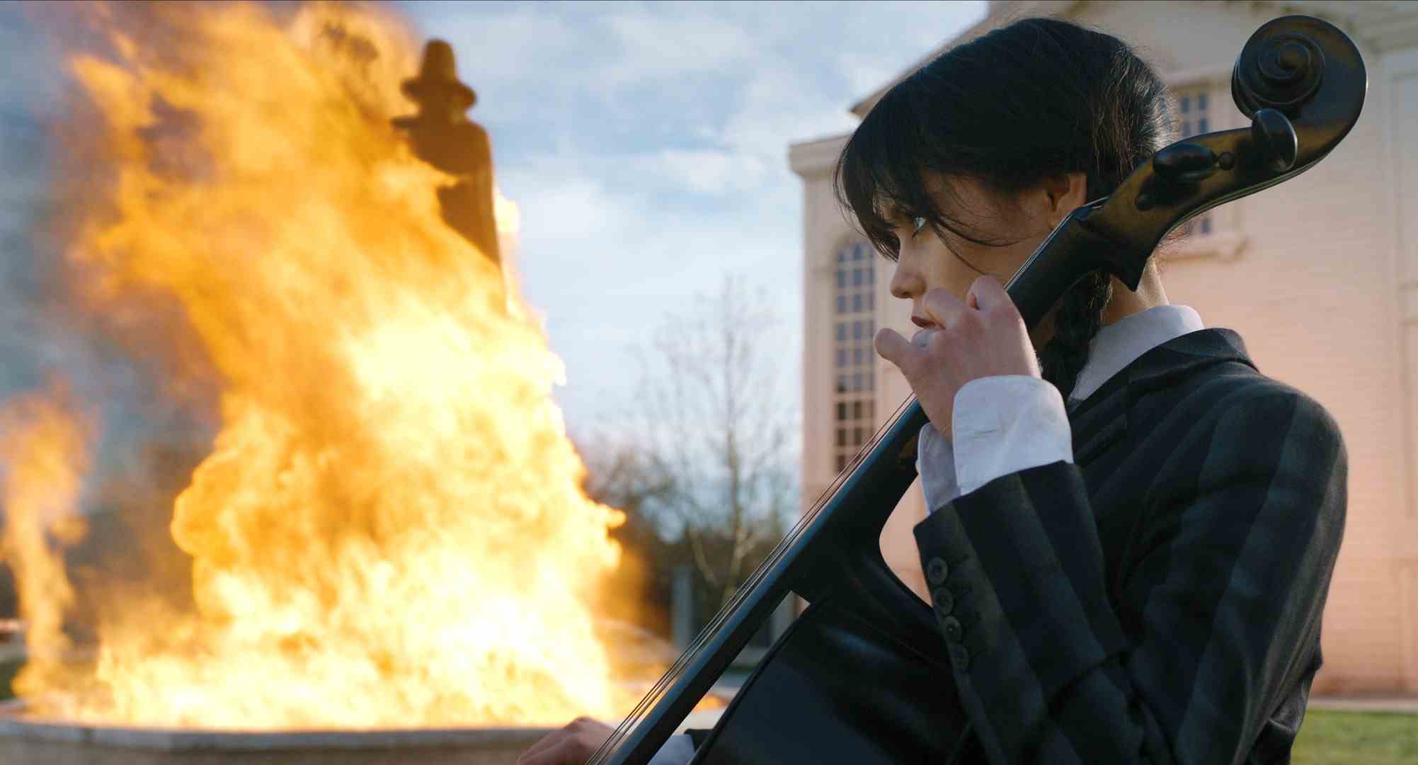 Wednesday Addams (Jenna Ortega) plays Cello while a fire blazes in the background