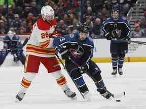 Johnny Gaudreau des Blue Jackets de Columbus, à droite, porte la rondelle à travers la ligne bleue devant Elias Lindholm des Flames de Calgary lors de la deuxième période d'un match de hockey de la LNH le vendredi 9 décembre 2022 à Columbus, Ohio.