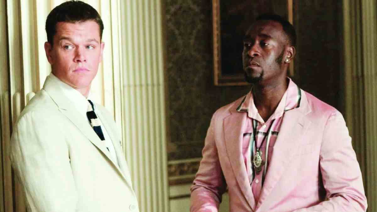 Matt Damon and Don Cheadle stand near each other dressed in suits in Ocean