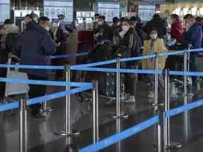 Des voyageurs masqués avec des bagages font la queue au comptoir d'enregistrement des vols internationaux à l'aéroport international de Beijing Capital à Pékin, le jeudi 29 décembre 2022.