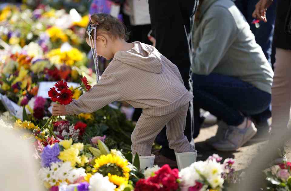 Un enfant dépose des fleurs à l'extérieur de Cambridge Gate lors de la longue promenade à Windsor avant les funérailles de la reine Elizabeth II lundi