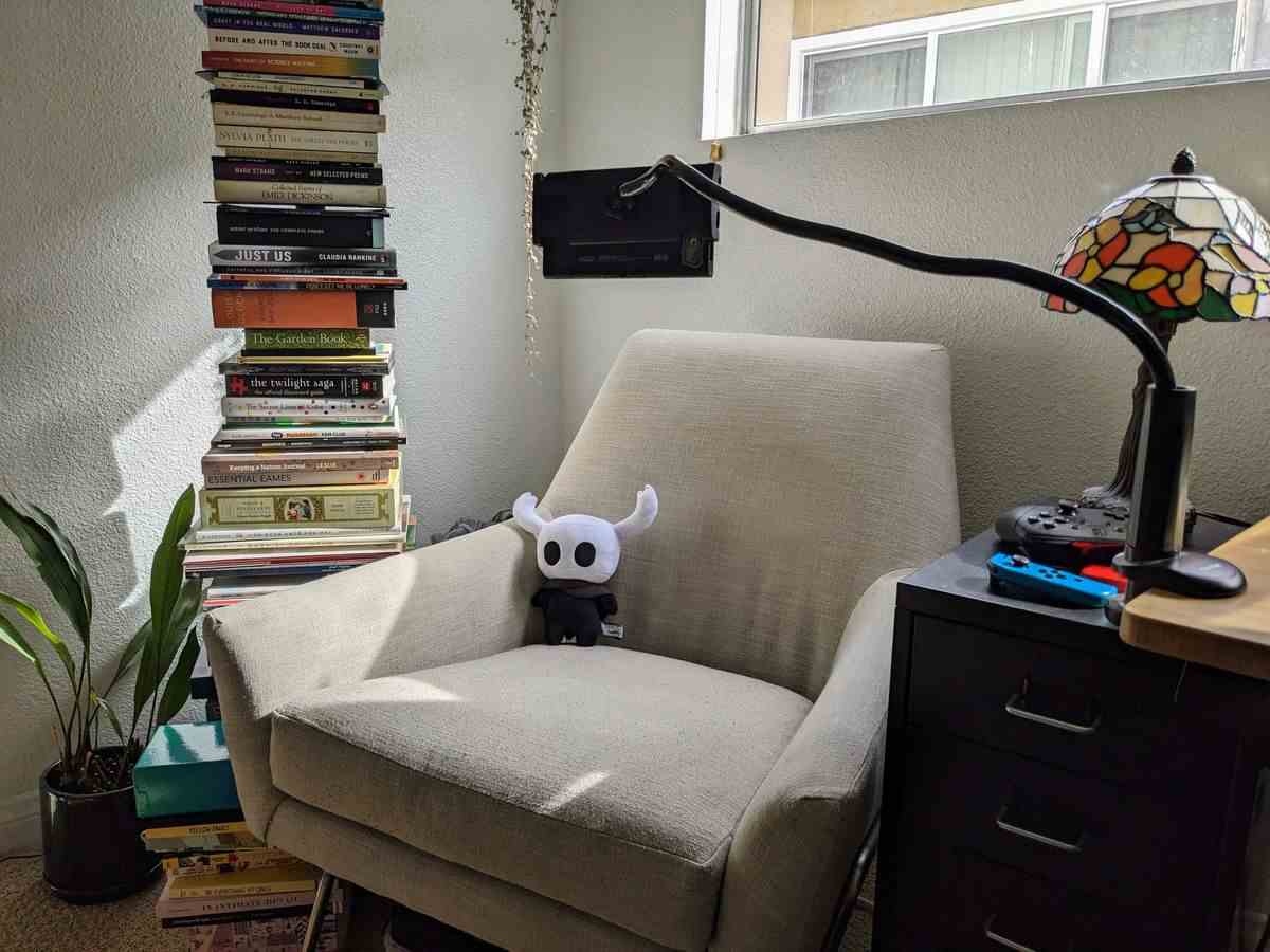 Un support pour tablette tient une Nintendo Switch face à un fauteuil.  Une peluche Hollow Knight est assise sur la chaise.