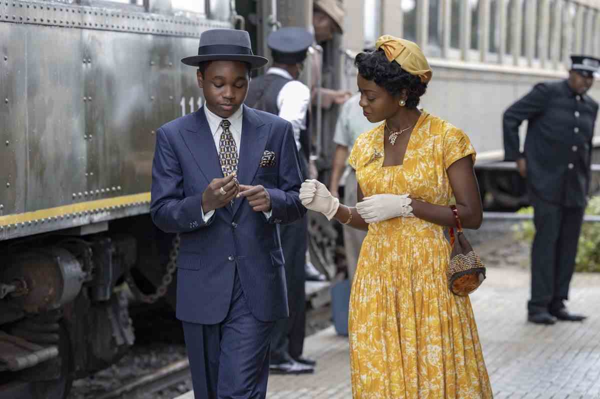 Un garçon en costume bleu marine (Jalyn Hall) se tient à côté d'une femme en robe jaune (Danielle Deadwyler) à côté d'une locomotive.