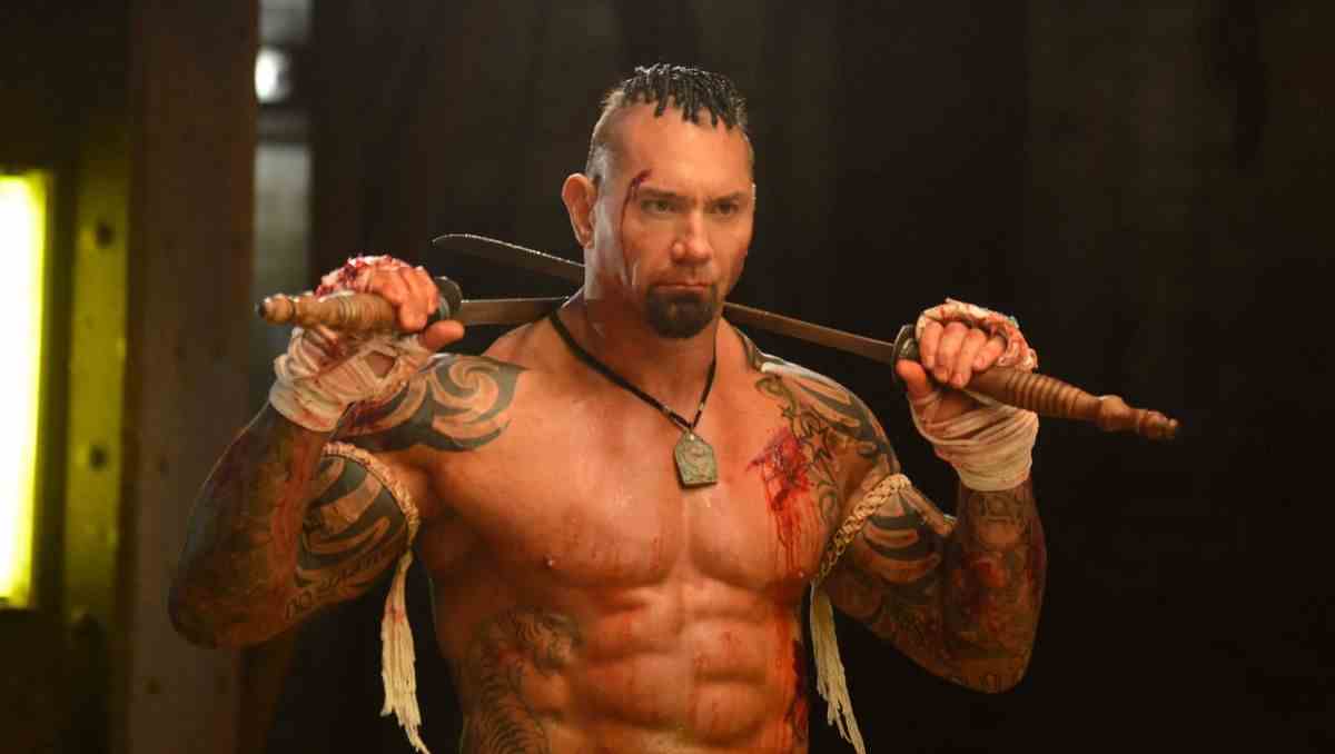 Dave Bautista, torse nu et avec du sang sur lui, tient deux épées sur ses épaules et a des bandes autour de ses mains dans Kickboxer : Vengeance