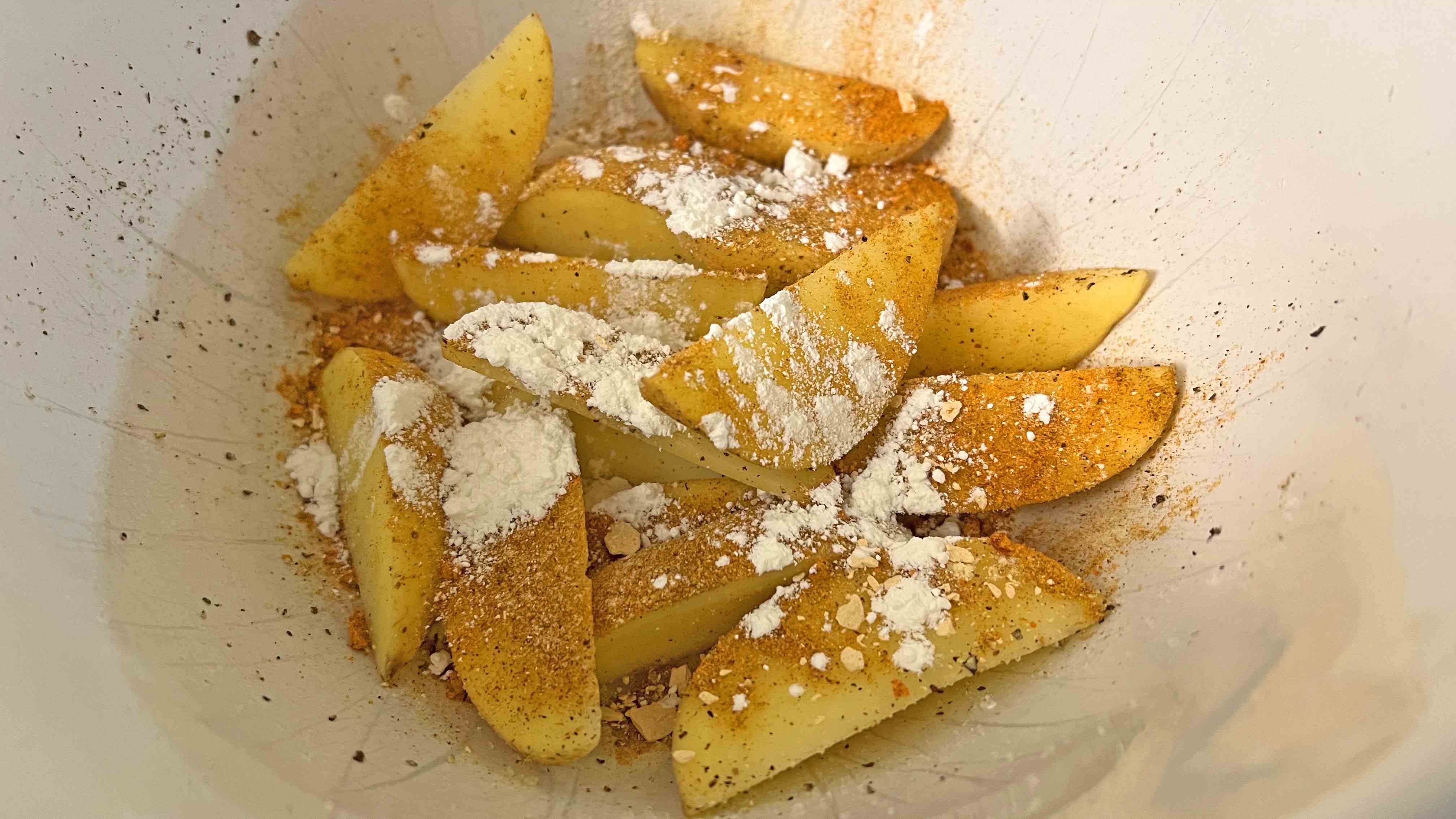 quartiers de pommes de terre dans un bol avec fécule de maïs, sel poivre et assaisonnement au paprika