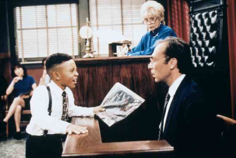 A child in a dress shirt, tie, and suspenders, yells at balding bespectacled adult man on the witness stand in a mock court; still from "Smart Guy"