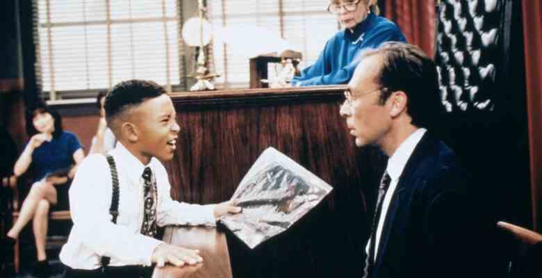 A child in a dress shirt, tie, and suspenders, yells at balding bespectacled adult man on the witness stand in a mock court; still from "Smart Guy"