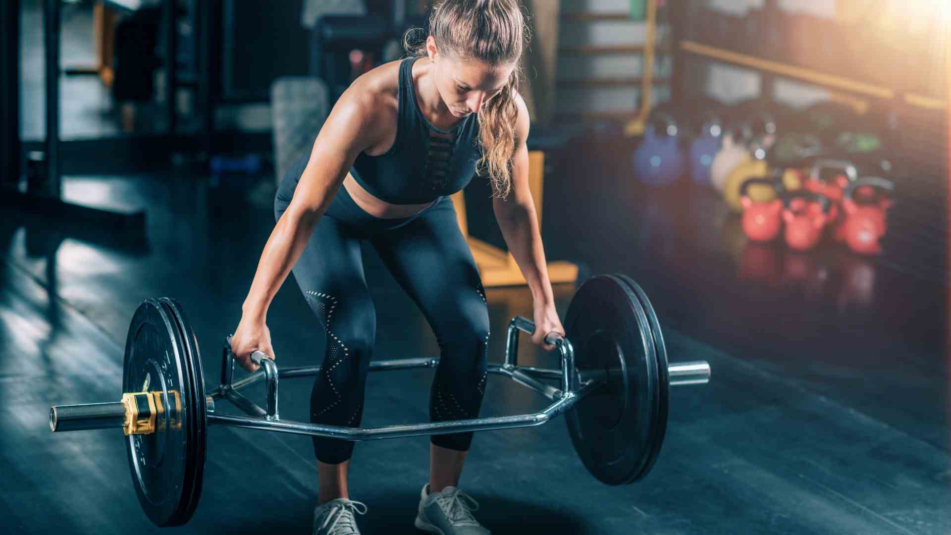 Femme exécutant un soulevé de terre à barre hexagonale dans une salle de sport