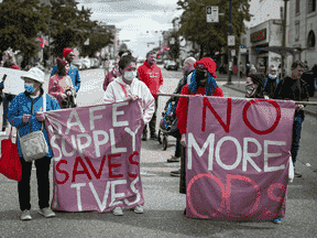 Les gens tiennent des banderoles lors d'une marche à Vancouver à l'occasion de la Journée internationale de sensibilisation aux surdoses pour se souvenir de ceux qui sont morts pendant la crise des surdoses et pour demander un approvisionnement sûr en drogues illicites.