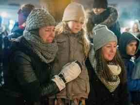 Un couple de femmes avec une fille pleure lors d'une veillée devant l'église Ste-Rose-de-Lima à Laval, au nord de Montréal, le jeudi 9 février 2023, à la mémoire des enfants tués lorsqu'un autobus de la ville a été conduit dans une garderie la veille .