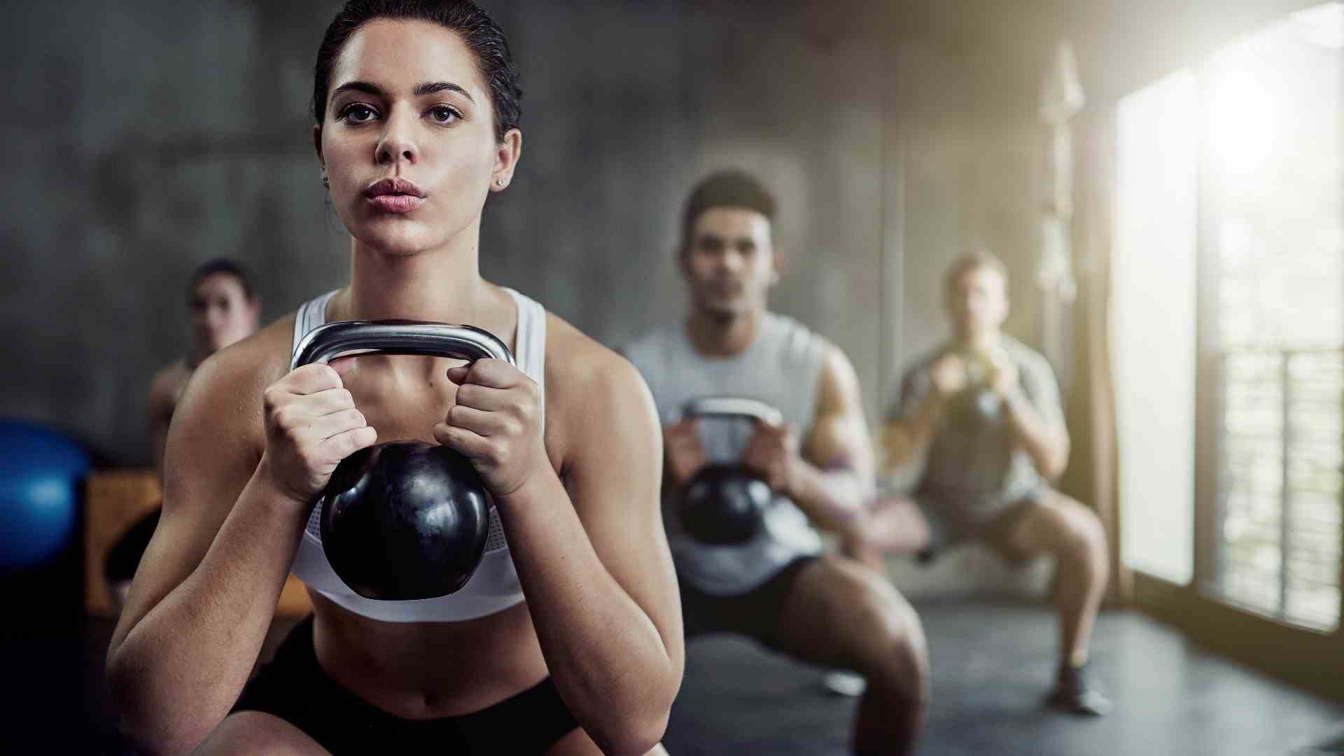 Meilleurs exercices de kettlebell : groupe effectuant un squat de gobelet tenant un kettlebell à deux mains