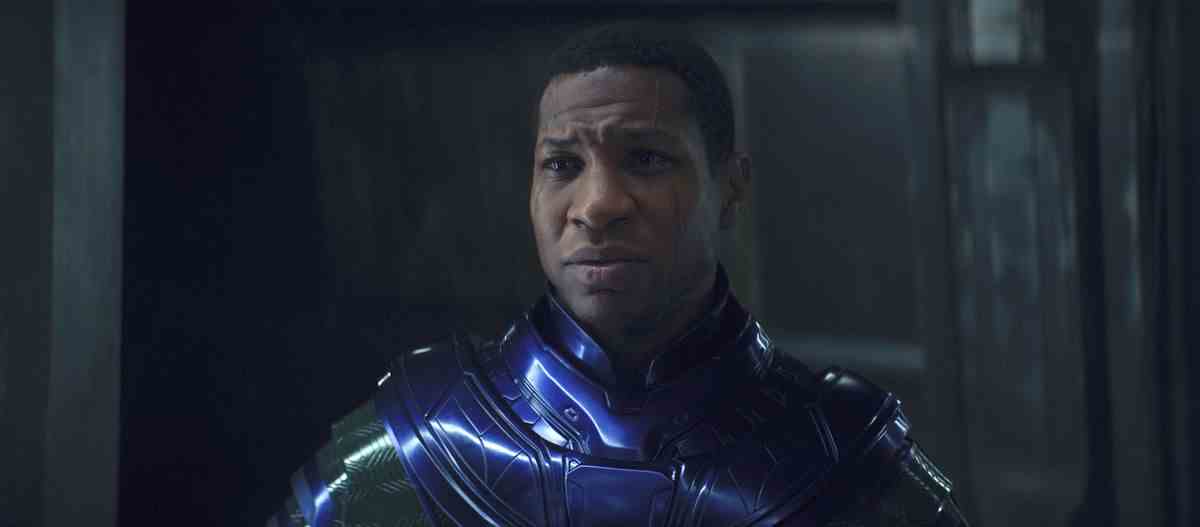 Jonathan Majors dans le rôle de Kang le Conquérant dans Ant-Man and the Wasp: Quantumania.  Il porte une combinaison de puissance brillante et gravée et triste.  Son visage a deux cicatrices qui vont de la racine des cheveux aux sourcils, puis de la joue à la mâchoire. 