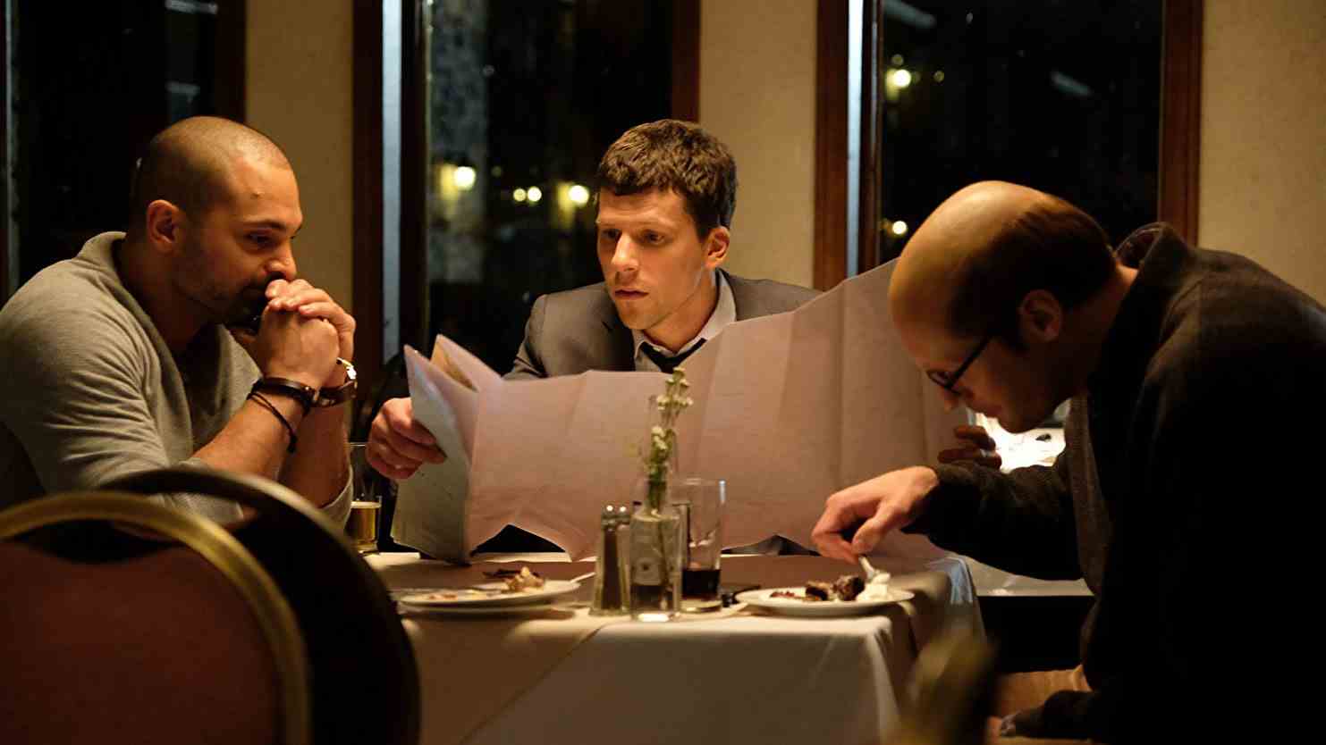 Jesse Eisenberg tient un menu à une table de restaurant