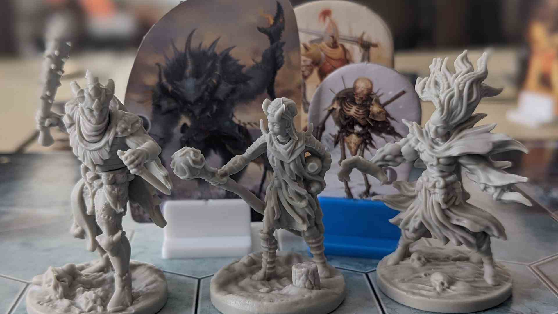 Trois figurines de Frosthaven sont alignées sur un tableau devant des monstres en carton