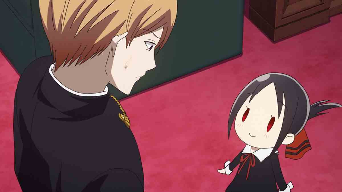 Le lycéen Miyuki Shirogane porte une expression déconcertée et une perle de sueur alors qu'il regarde une version chibi souriante de son béguin Kaguya Shinomiya dans Kaguya-sama: Love is War - Le premier baiser qui ne finit jamais