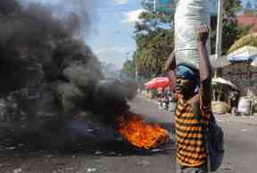 Un marchand marche près d'une barricade en feu alors que des manifestants organisent une manifestation demandant justice pour les policiers tués par des gangs armés, à Port-au-Prince, Haïti, le 27 janvier 2023.