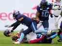 Le casque du receveur des Alouettes de Montréal, Eugene Lewis, s'envole après avoir été taclé par les arrières défensifs des Argonauts de Toronto, Robert Priester, à droite, et Royce Metchie lors de la finale de la deuxième moitié de l'Est de la LCF à Toronto le 13 novembre 2022.