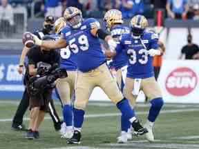 Le demi-centre Andrew Harris (à droite) des Blue Bombers de Winnipeg fait de l'ombre à l'OL Michael Couture après lui avoir remis le ballon pour célébrer son touché au sol contre les Stampeders de Calgary lors de la saison 2021.  Couture s'est officiellement joint aux Lions de la Colombie-Britannique en tant qu'agent libre mardi.