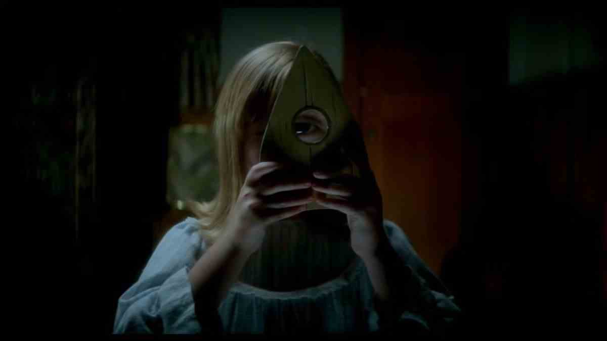 Une jeune fille regarde à travers une planchette ouija dans Ouija: Origin of Evil