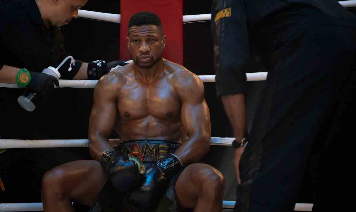 Damian (Jonathan Majors) affalé dans le coin d'un ring de boxe pendant un match, torse nu et en sueur, alors que les préposés lui offrent une bouteille d'eau et se penchent pour s'entretenir avec lui dans Creed III