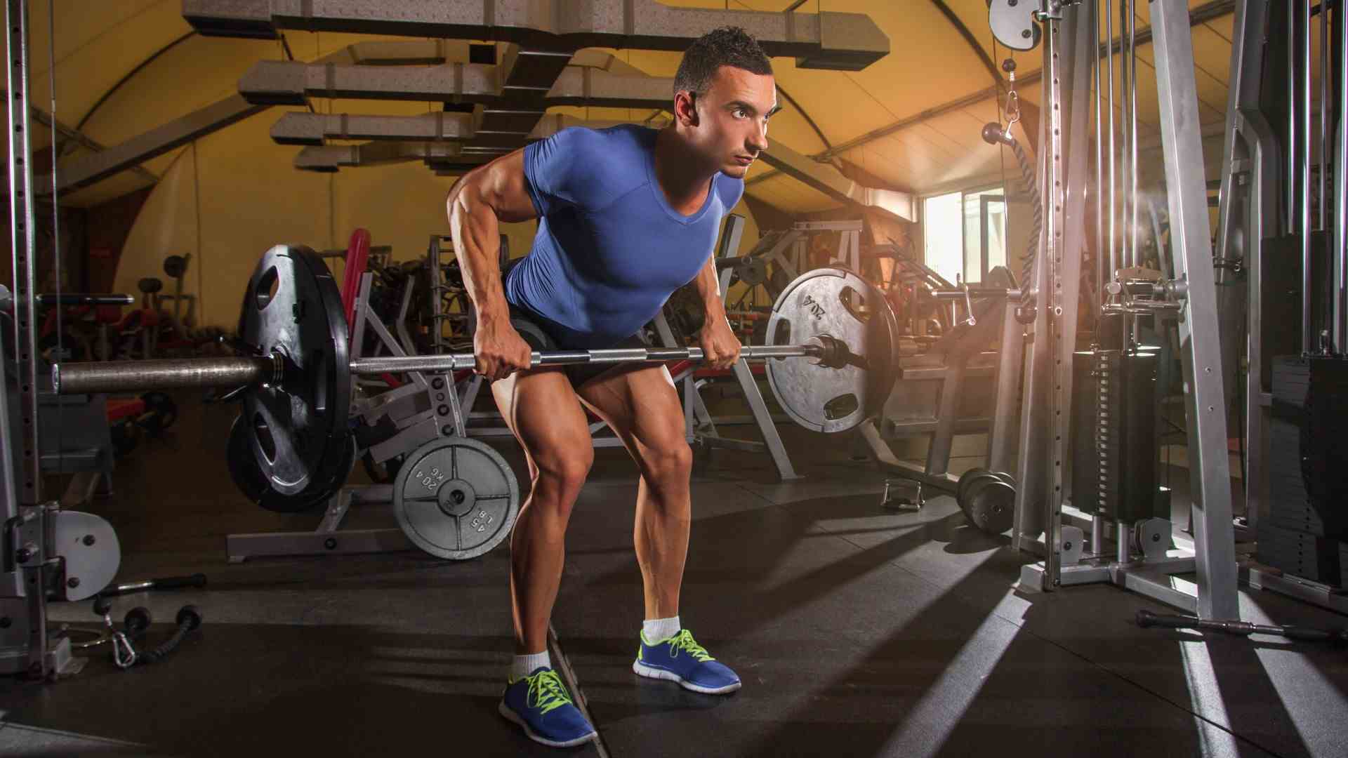 Homme exécutant une rangée penchée d'haltères dans la salle de sport avec la barre relevée en position rangée contre son estomac