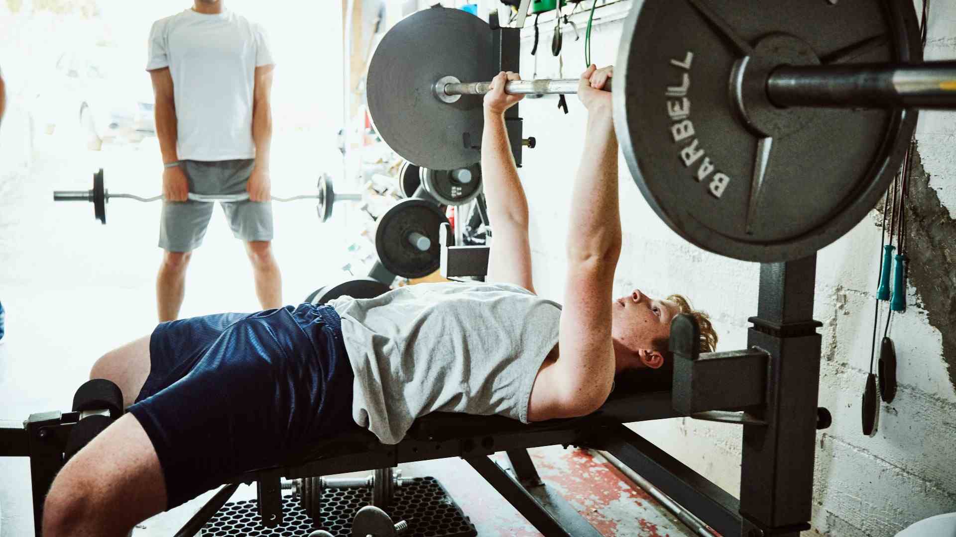 Homme exécutant un développé couché à la barre avec la barre posée sur le rack de squat et les bras tendus, les mains agrippant la barre