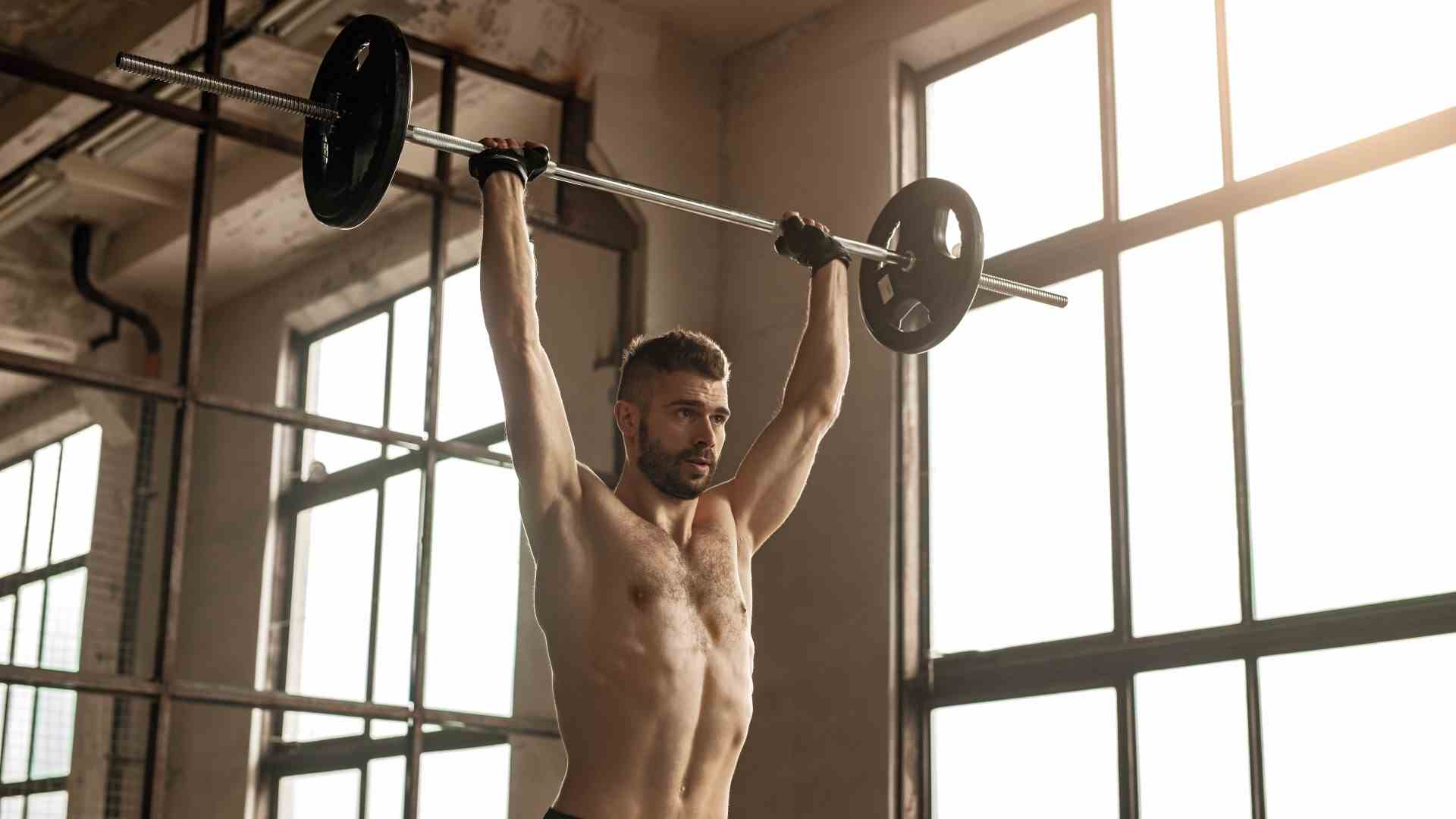 Homme exécutant une presse aérienne d'haltères avec la barre étendue au-dessus de sa tête dans la salle de gym