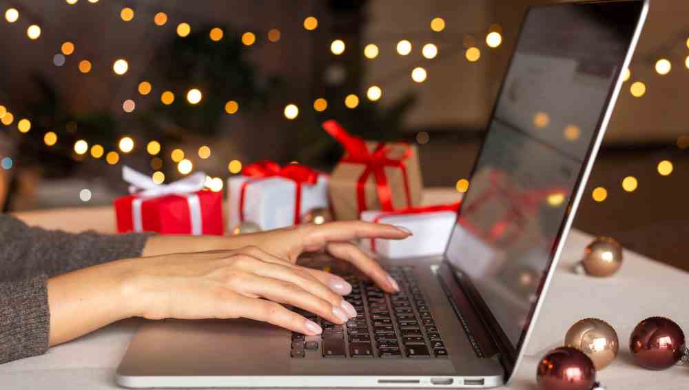 Les mains de la femme tapent sur MacBook avec un sapin de Noël et des décorations de vacances tout autour.