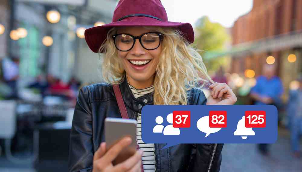 Femme blonde souriante portant des lunettes et un chapeau souple regardant son téléphone avec des icônes de notification Facebook superposées sur l'image.